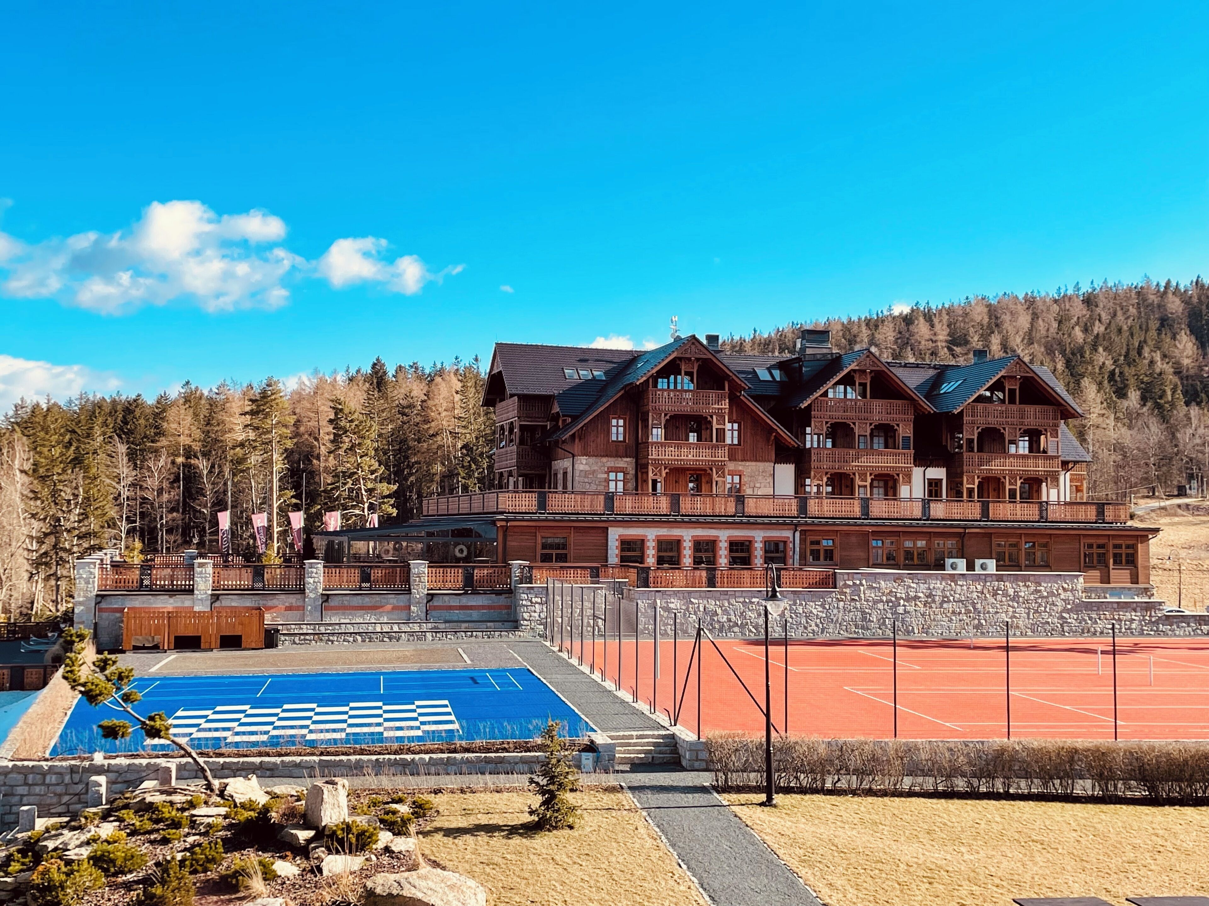 A large wooden building with multiple balconies, a tennis court, and a pool area.