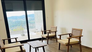 A room with wooden flooring, a large sliding glass door, and two wooden chairs with cushions.