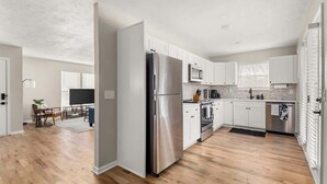 A modern kitchen with white cabinets, stainless steel appliances, and a wooden floor. - Backstage Bungalow- Cozy 3BR Retreat in The Nations + Near Downtown (Nashville)