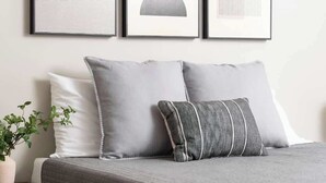 A neatly made bed with grey bedding and pillows, a small bedside table with a plant, and framed artwork on the wall. - Backstage Bungalow- Cozy 3BR Retreat in The Nations + Near Downtown (Nashville)