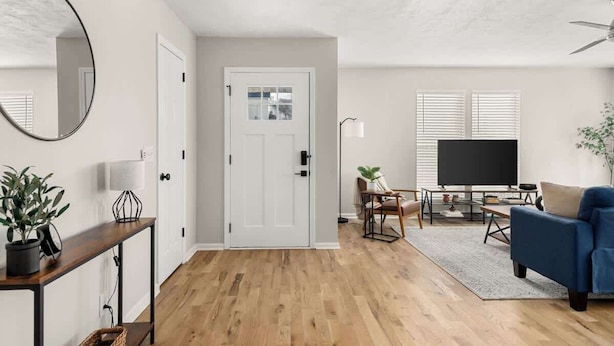 A modern living room with a wooden floor, a blue sofa, a TV, and a dining area with a table and chairs. - Backstage Bungalow- Cozy 3BR Retreat in The Nations + Near Downtown (Nashville)