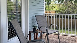A covered porch with two chairs and a small table, a white railing, and a view of trees and a wooden fence. - Backstage Bungalow- Cozy 3BR Retreat in The Nations + Near Downtown (Nashville)