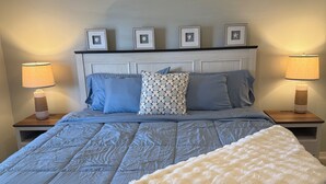 Ein Schlafzimmer mit einem Bett, zwei Nachttischen, einem Deckenventilator und gerahmten Bildern am Kopfteil.