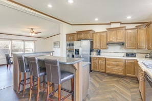 A kitchen with wooden cabinets, a central island with bar stools, a refrigerator, and a microwave. - Fish & Relax Fireside: Mink Lake Retreat! (Buffalo)
