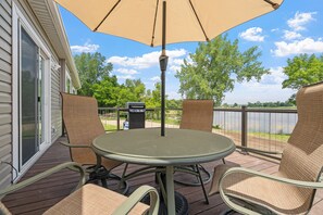 A patio with a round table and chairs, an umbrella, and a view of a lake.