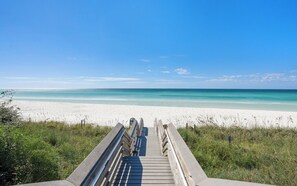 Une promenade en bois qui mène à une plage où l’eau est d’un bleu limpide et le sable est blanc.