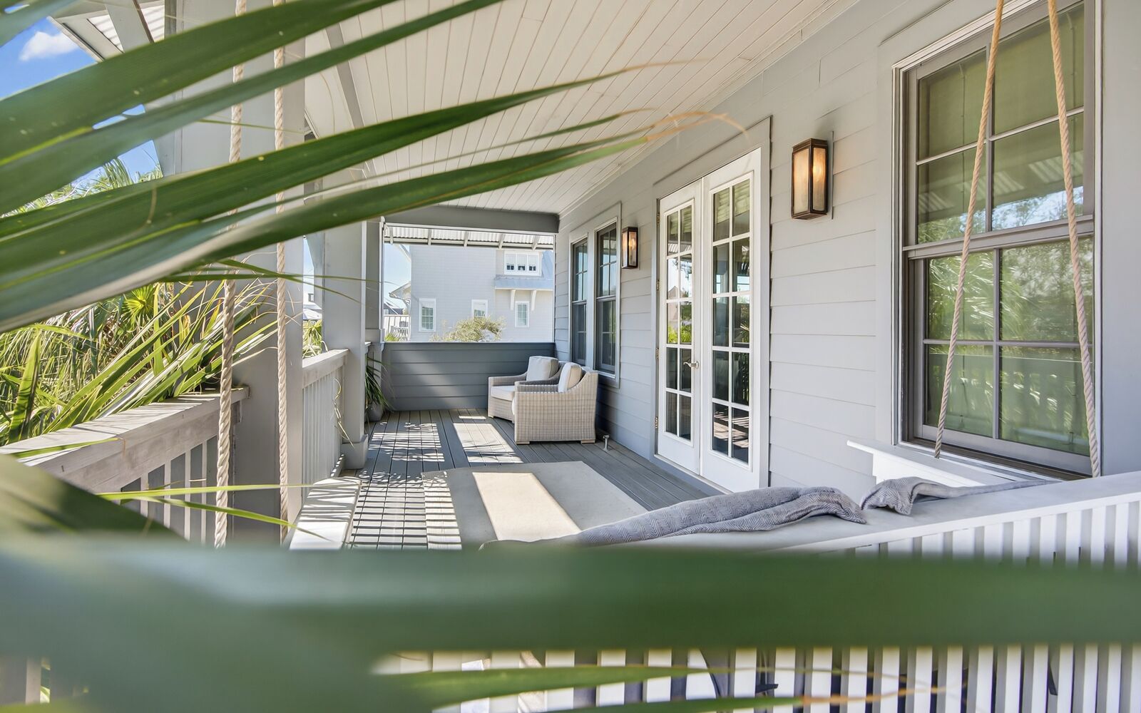 A covered porch with a sofa and a bench, white railings, and a view of a building in the background.