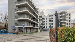 Un edificio residencial de varios pisos con balcones, una zona de estacionamiento y una entrada con portón.