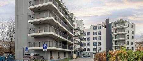A multi-story residential building with balconies, a parking area, and a gated entrance.