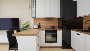 Una cocina moderna con armarios blancos, encimera de madera, horno empotrado y salpicadero negro.