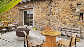 Un bâtiment en pierre avec une table et des chaises en bois, un foyer et un banc.