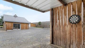 A covered outdoor area with a gravel floor, a wooden building, and a dartboard mounted on a wooden wall.