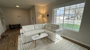 Uma sala de estar moderna com um sofá modular, uma mesa de centro e uma janela grande com vista para a rua.