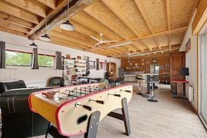 A spacious room with a foosball table, wooden ceiling beams, and a kitchen area in the background. - Le Nid Longère – Studio and Living Area (ABBARETZ)