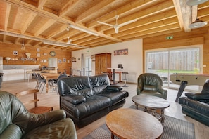 A spacious living area with a wooden ceiling, leather sofas, a dining table, and a pool table.