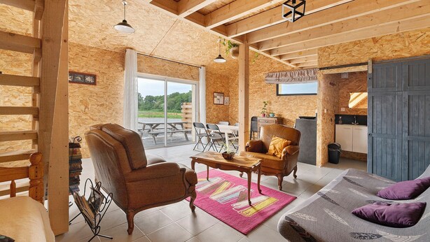 A wooden interior with a sofa, armchair, dining table, and a view of the outdoors.