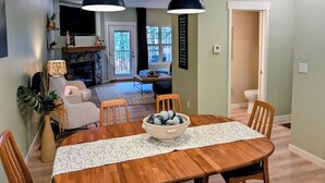 A dining area with a wooden table, chairs, and a bowl of decorative items. There is a television and a fireplace in the background. - Chalet 113 at the Official Collins Lake Resort (Government Camp)
