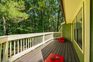 Eine Holzterrasse mit weißer Brüstung, einer roten Bank und einem Gebäude mit großen Fenstern in Grün.