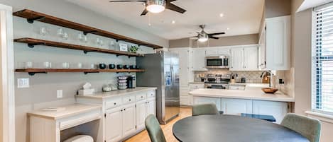 A modern kitchen with white cabinets, a central island, and a dining area with green chairs.