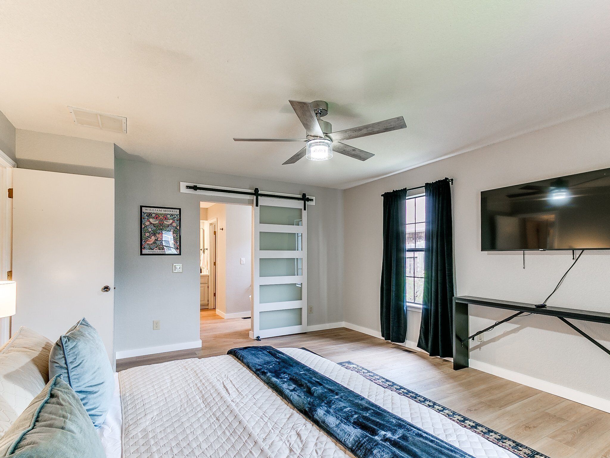 A bedroom with a bed, a ceiling fan, a TV, and a sliding door leading to a bathroom.