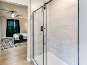 Un dormitorio moderno con cabina de ducha de vidrio, una cama con cubrecama verde oscuro y un ventilador de techo.