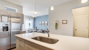 Een moderne keuken met een roestvrijstalen koelkast, een dubbele spoelbak, houten kastjes en hanglampen.