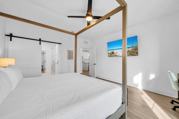 Un dormitorio moderno con una cama con dosel, un ventilador de techo y una pintura de una playa.