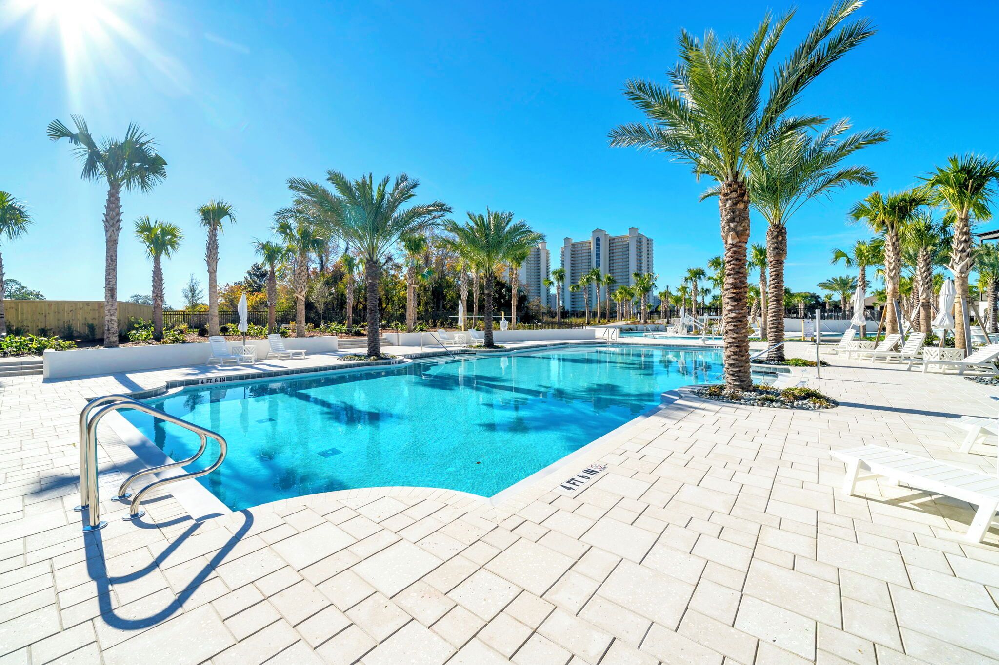 A swimming pool with palm trees, lounge chairs, and a clear blue sky.