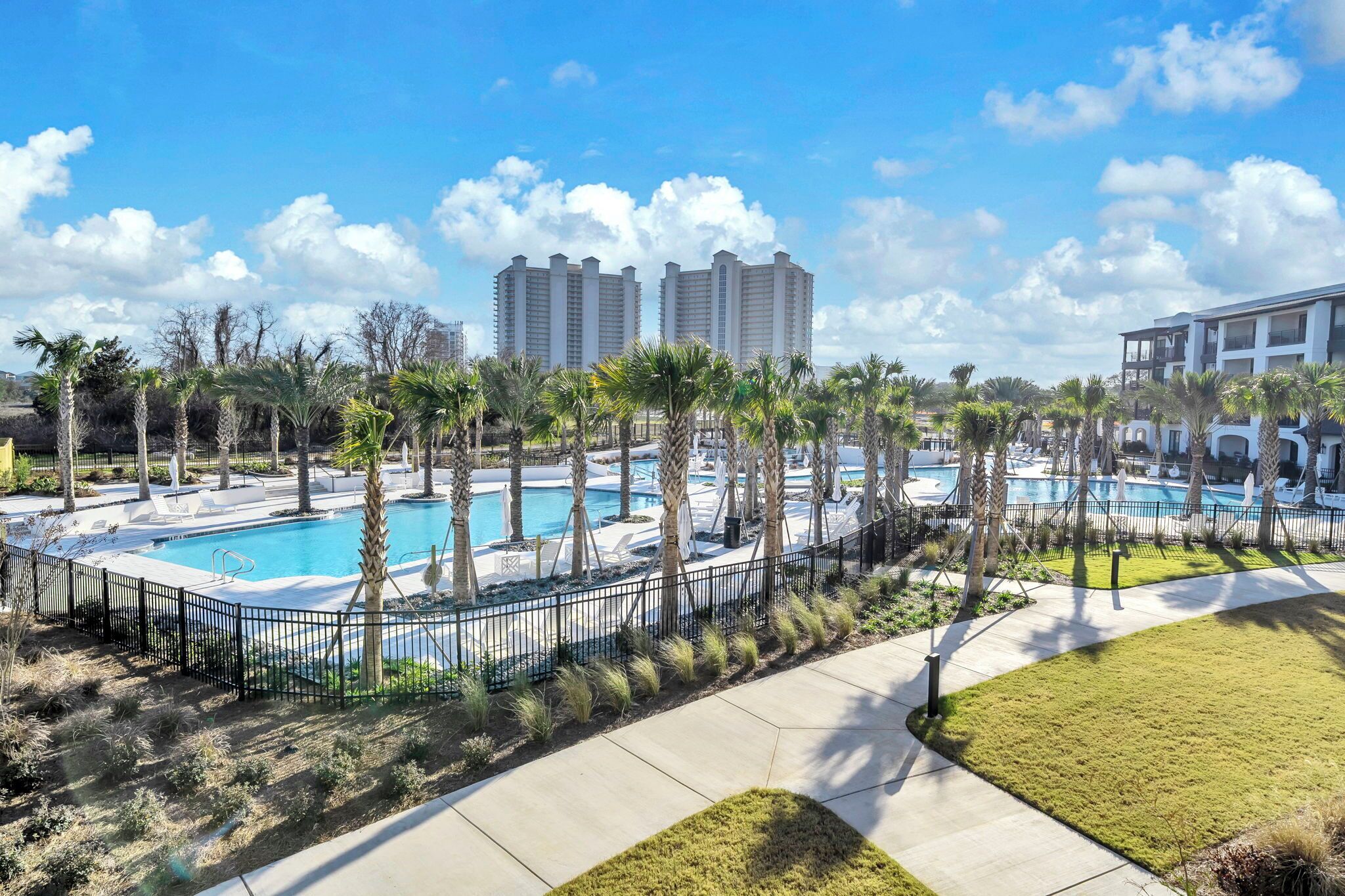 A pool area with palm trees, a fenced pool, and a clear sky.