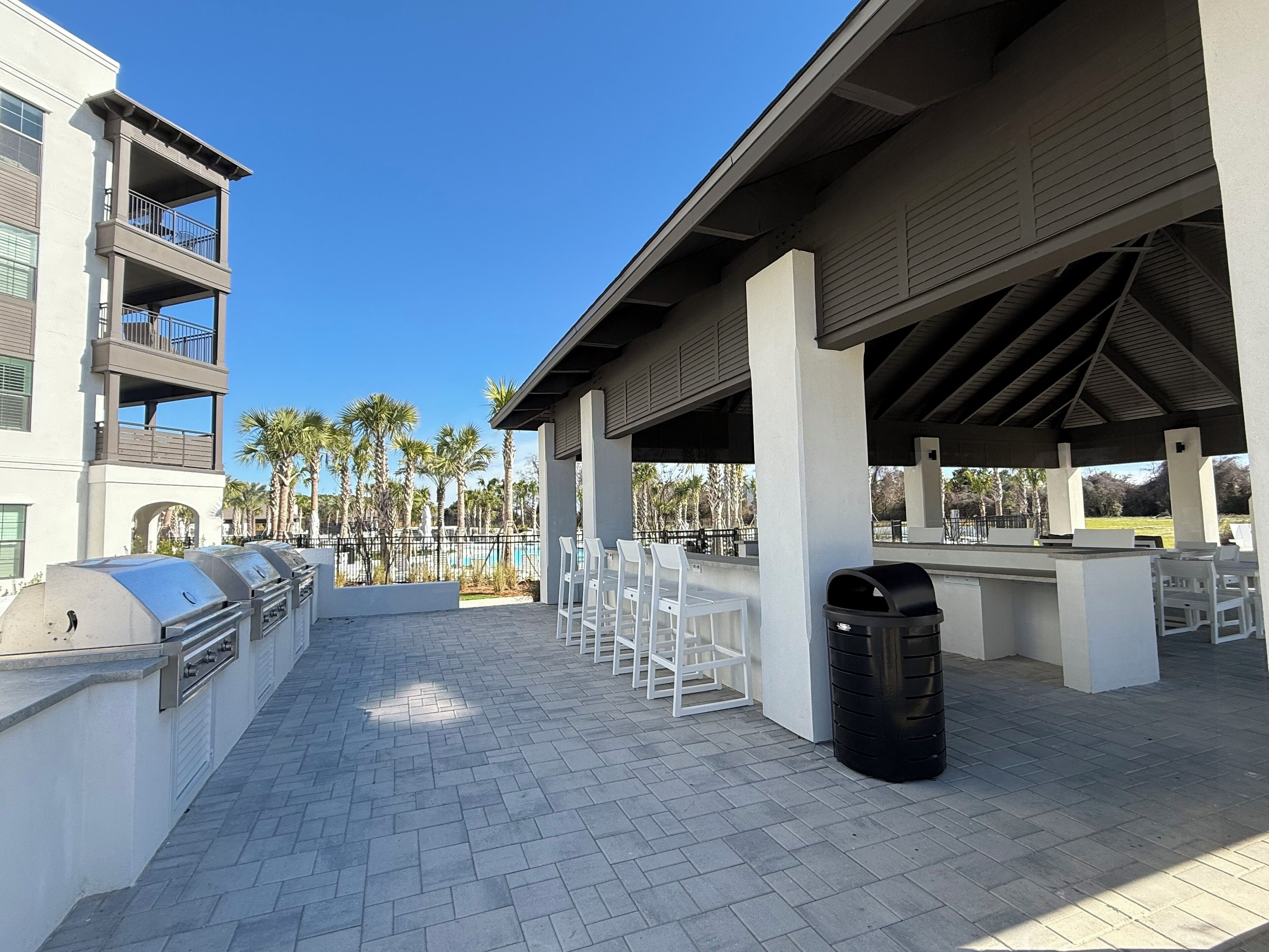 An outdoor patio area with barbecue grills, white plastic chairs, and a trash can.