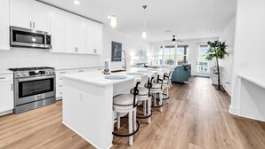 A modern kitchen with white cabinetry, stainless steel appliances, and a central island with bar stools. - The Grove Juniper 228 - 2 Bedrooms - Lazy River - Seascape Resort (Miramar Beach)