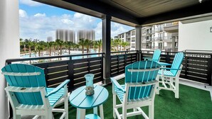 A balcony with turquoise chairs and a small table, overlooking a pool and high-rise buildings. - The Grove Juniper 228 - 2 Bedrooms - Lazy River - Seascape Resort (Miramar Beach)