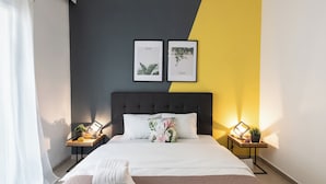 Ein ordentlich bezogenes Bett mit weißen Leinen, einem grauen Kopfteil und zwei gerahmten Naturmotiven an der Wand.