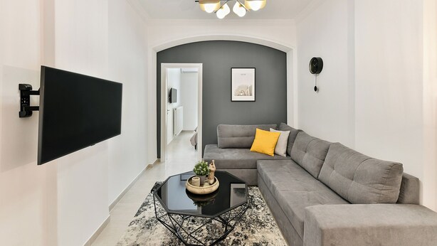 Ein modernes Wohnzimmer mit einem grauen Sofa, einem schwarzen Couchtisch und einem an der Wand befestigten Fernseher.