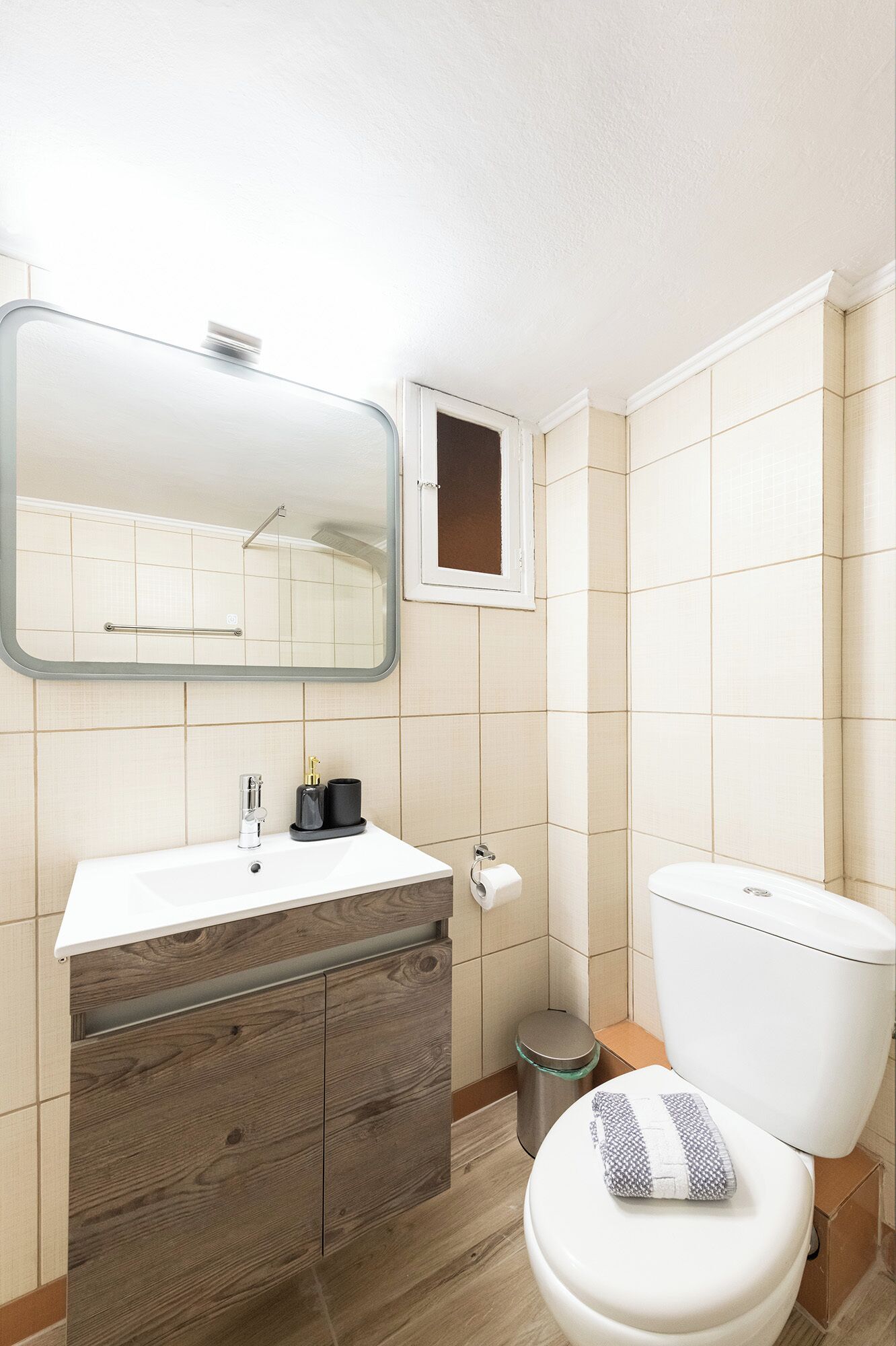Een moderne badkamer met een houten wastafel, een spiegel, een toilet en een prullenbak.