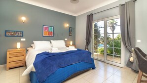 Un dormitorio con cama, mesitas de noche, decoración en la pared y una puerta corrediza de vidrio a un balcón.