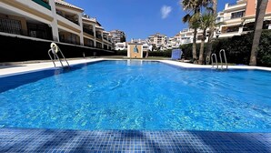 A clear blue swimming pool with a tiled edge, surrounded by multi-story buildings with balconies and palm trees. - Euromar 121 (Torrox)