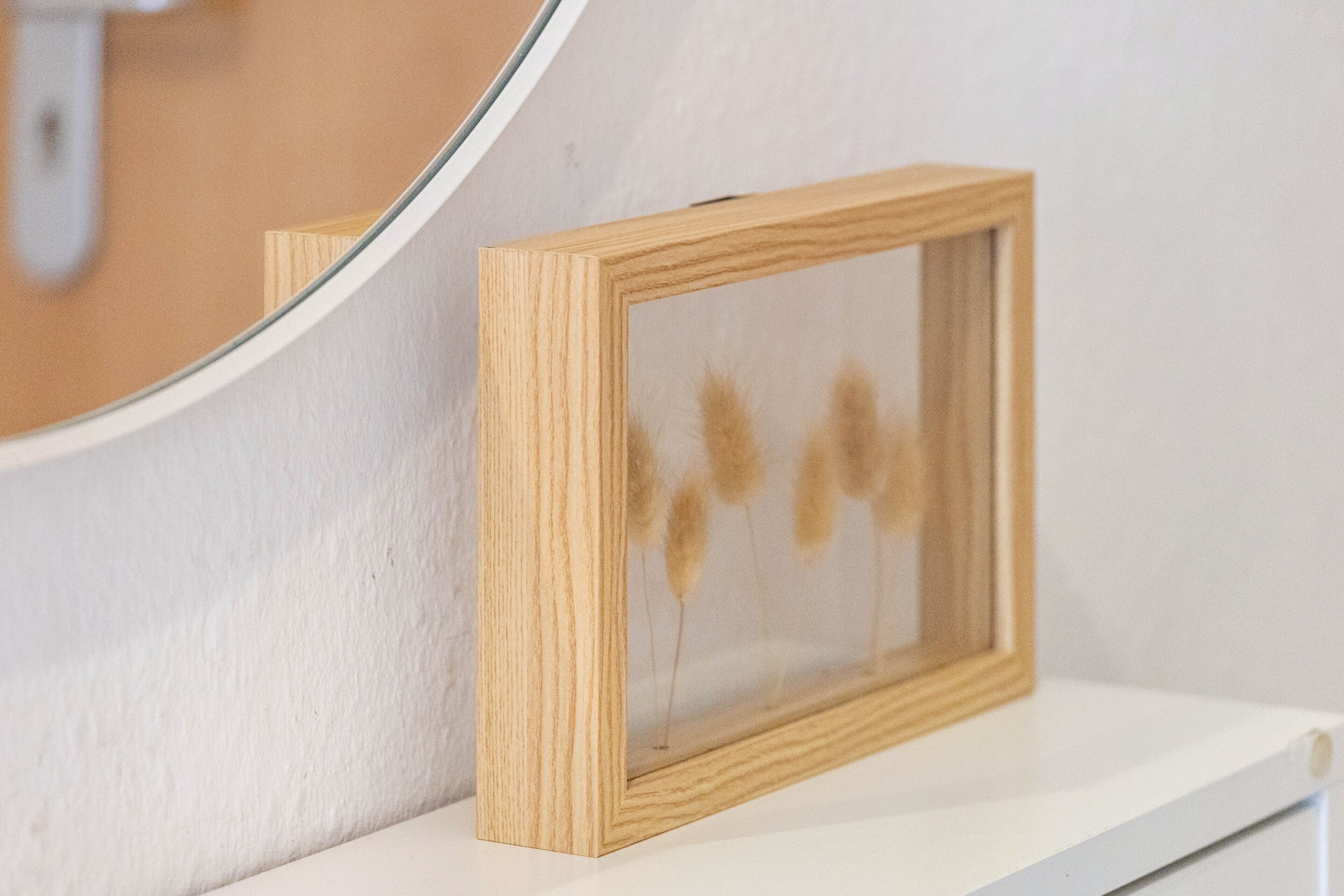 Ein Bilderrahmen aus Holz mit getrockneten Pflanzen auf einem weißen Regal.