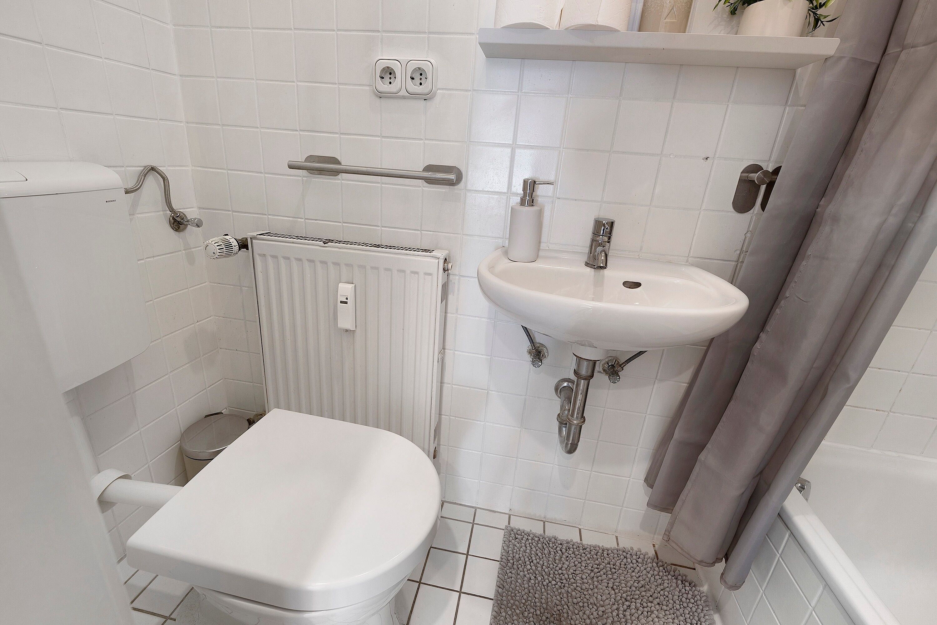 Ein Badezimmer mit Toilette, Waschbecken, Duschvorhang und Heizkörper.