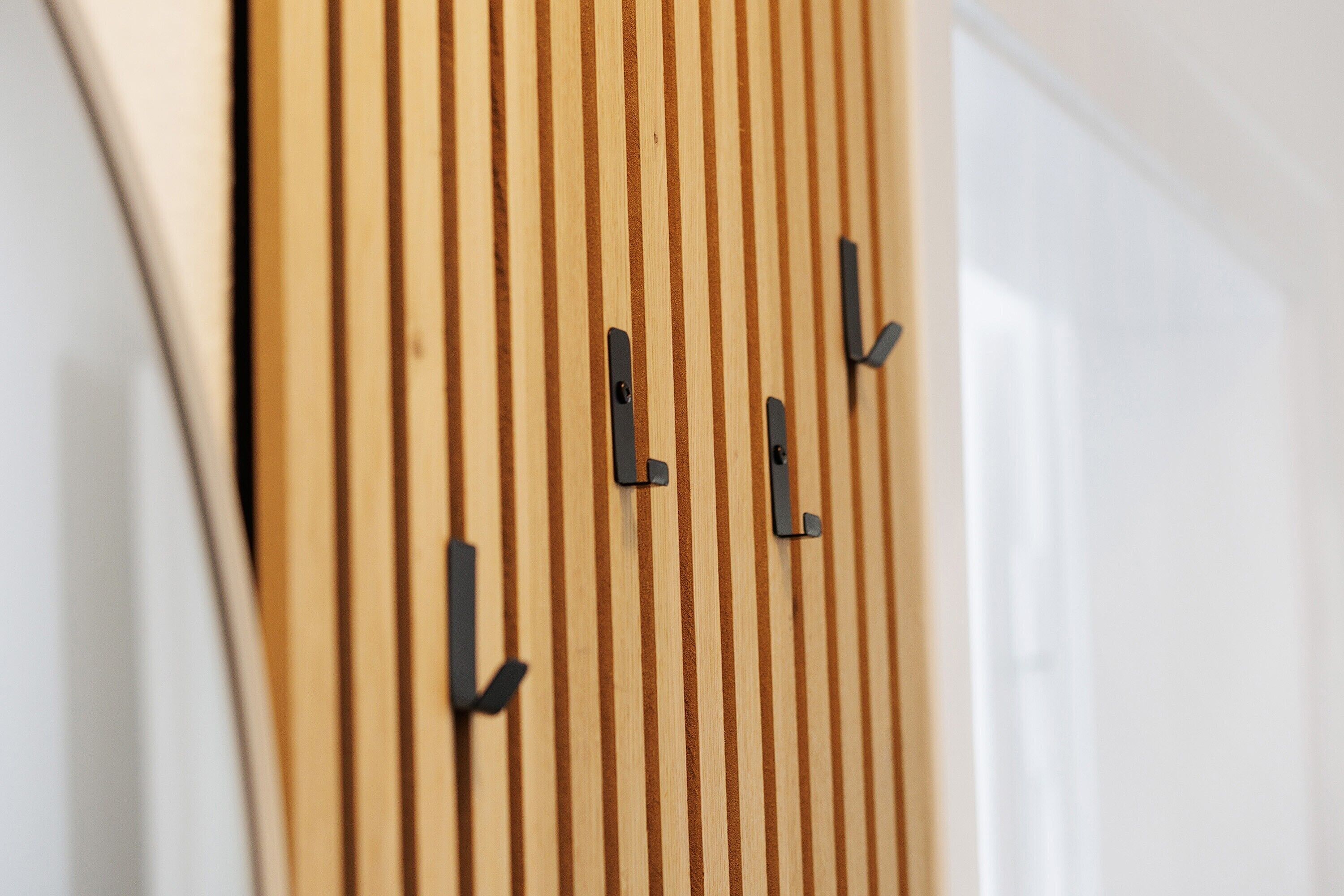 Eine Holzverkleidung mit vertikalen Linien und schwarzen Haken.
