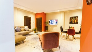 A modern living room with a sofa, a red chair, a TV, and a dining area with chairs and a table. - Spacious 3-bedroom house in Accra (Achimota)