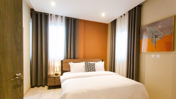 A hotel room with a large bed, a nightstand, a lamp, and a painting on the wall. - Spacious 3-bedroom house in Accra (Achimota)
