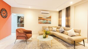 A modern living room with a beige sofa, a round coffee table, and a red armchair. - Spacious 3-bedroom house in Accra (Achimota)