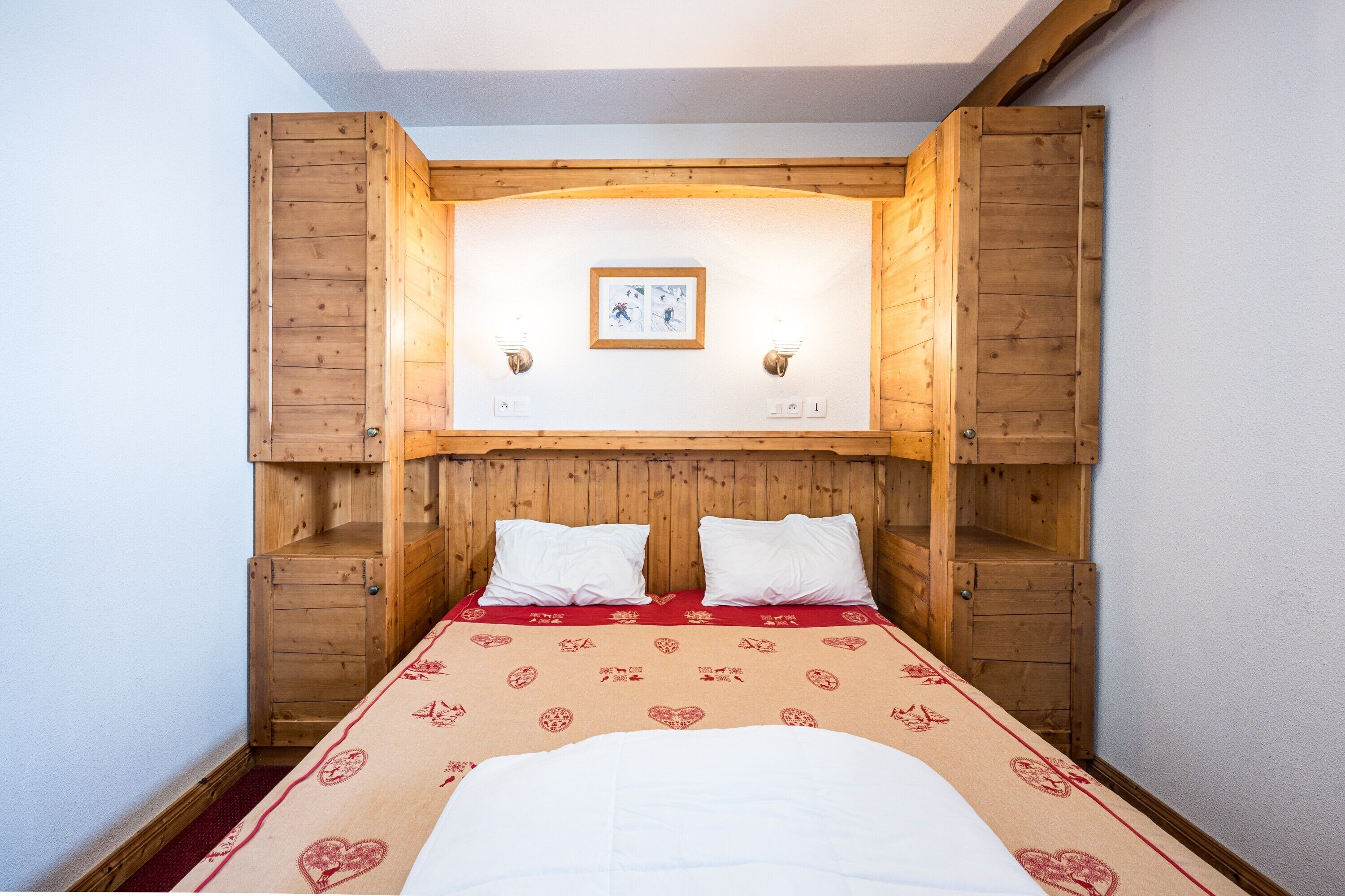 Une pièce aux murs en bois, avec un lit, deux lampes fixées au mur et un tableau encadré accroché au mur.