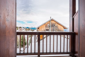 A wooden cabin with a balcony, snow-covered ground, and mountains in the background. - Relaxing Duplex with Pool in the Mountains (Fontcouverte-la-Toussuire)