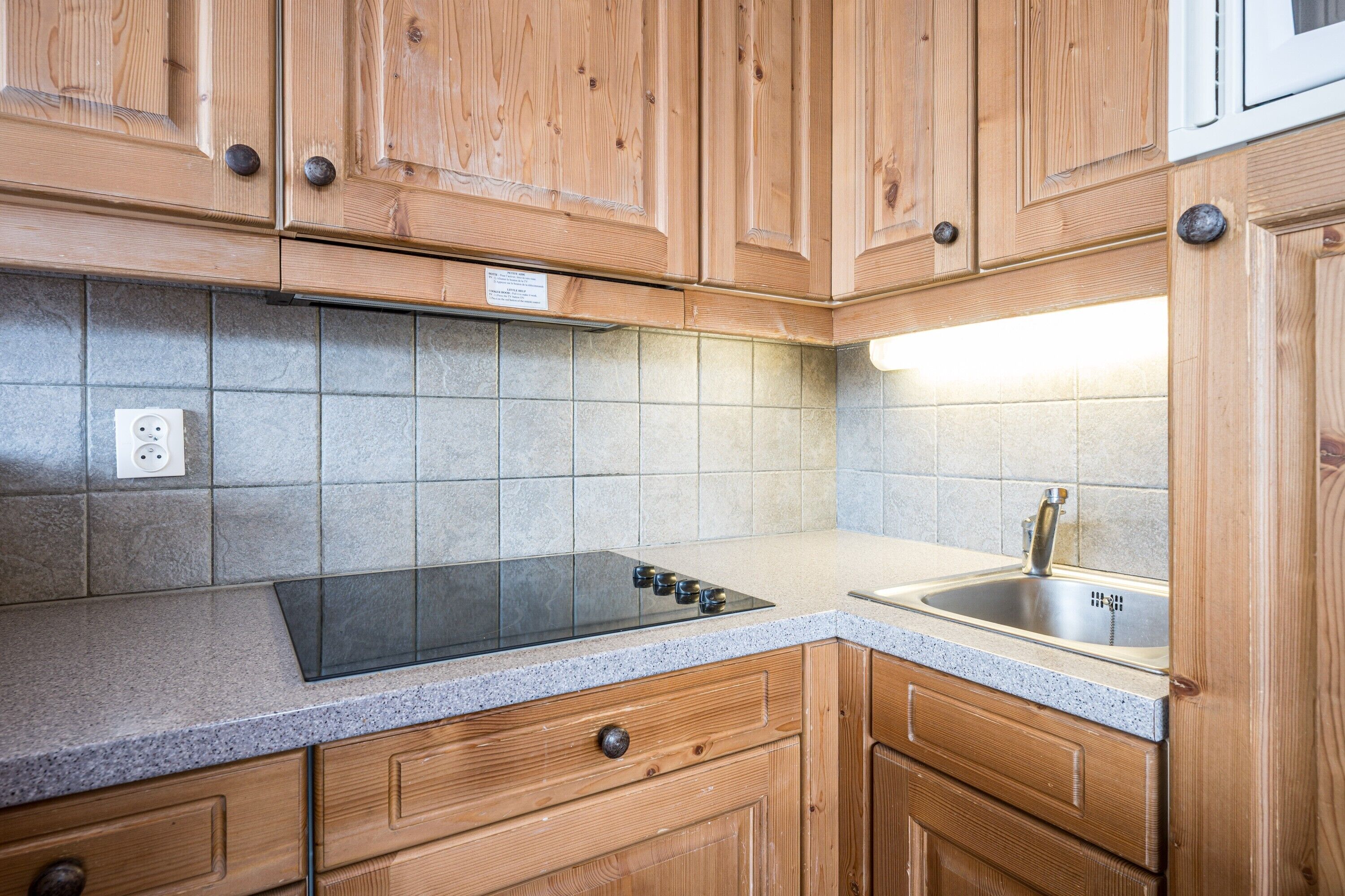 Eine Küche mit Holzausstattung, einem Edelstahlspülbecken, einem eingebauten Herd und einer gefliesten Spritzschutzwand.