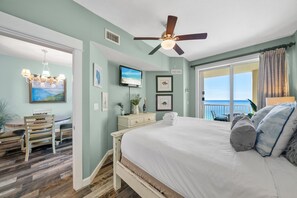 Ein Schlafzimmer mit Bett, Deckenventilator, Fernseher, Esstisch mit Stühlen und Meerblick vom Balkon.