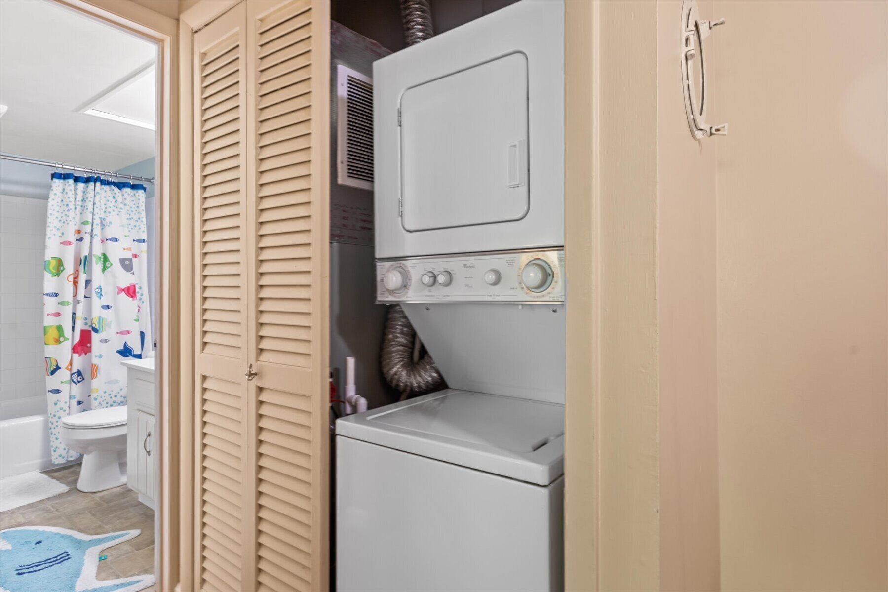 A compact laundry area with a washing machine and dryer, a toilet, and a shower curtain with a fish pattern.
