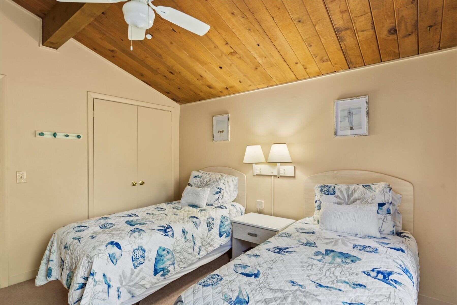 Une chambre avec deux lits, des poutres apparentes en bois au plafond, une porte et des lampes fixées au mur.