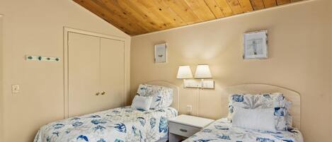 Une chambre avec deux lits, des poutres apparentes en bois au plafond, une porte et des lampes fixées au mur.